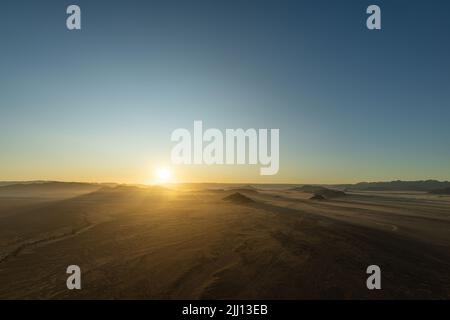 Alba vista da una mongolfiera durante un giro a Sossusvlei, Namibia. I raggi si illuminano sulle colline e le montagne del deserto del Namib. Foto Stock