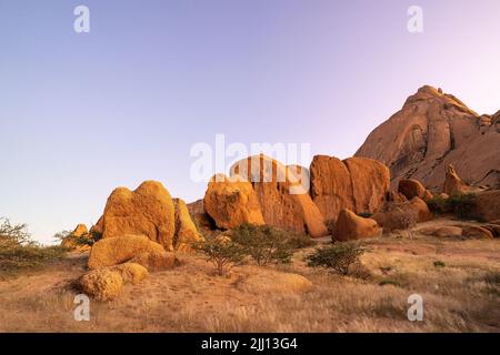 Grandi massi in primo piano e lo Spitzkoppe sullo sfondo all'alba con un bel cielo viola senza nuvole. Namibia campeggio in beautifu Foto Stock