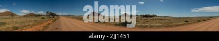 Una foto panoramica di una strada di ghiaia nel mezzo della Namibia. Cairns con grandi massi a metà distanza, cielo blu con nuvole bianche sparse. Foto Stock