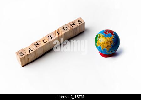Lettere di legno che formano la parola sanzioni e un globo in miniatura su uno sfondo bianco Foto Stock