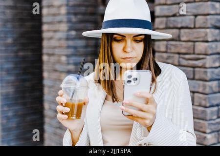 Bella donna che va a incontrare con caffè freddo e tenere il telefono a piedi per la strada. Ritratto di successo donna di affari che tiene la tazza di co Foto Stock