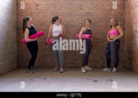 Un gruppo diversificato di giovani e attraenti donne sportive di diverse forme del corpo si riuniscono e parlano mentre si aspetta in palestra. Parete di mattoni industriali di fondo. Foto di alta qualità Foto Stock