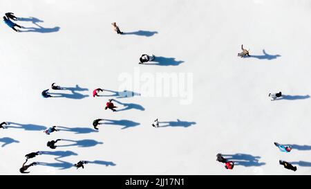 Molte persone stanno pattinando su una pista di ghiaccio bianca all'aperto in città in una soleggiata giornata invernale. Ombre di persone che pattinano sulla superficie di una pista di ghiaccio bianca. Vista aerea del drone. Vista dall'alto. Stile di vita, sport, riposo Foto Stock