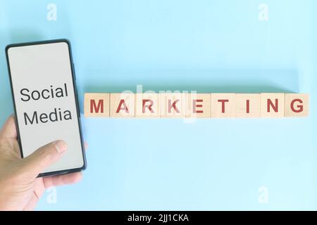 Concetto di strategia aziendale per il marketing dei social media. Telefono cellulare portatile con blocchi di legno su sfondo blu. Foto Stock