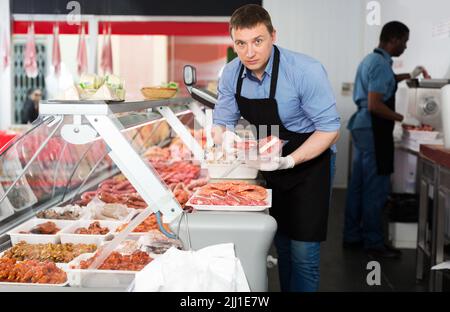 macellaio che organizza prodotti a base di carne in vetrina Foto Stock