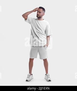 Mockup tuta con grinze bianche, t-shirt oversize, shorts su un ragazzo con barba, in sneakers, raddrizzando i capelli, isolato sullo sfondo, vista frontale. Foto Stock