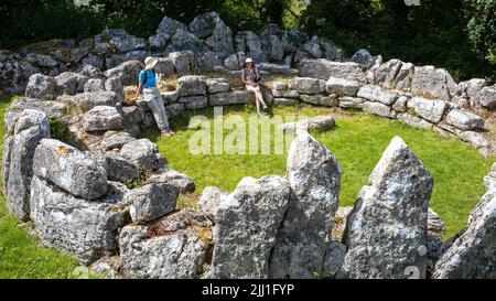 Visitatori del 21st ° secolo che riposano sulle fondamenta dell'età del ferro di un rifugio-cerchio a DIN Lligwy, Moelfre, Anglesey, Galles, Regno Unito Foto Stock