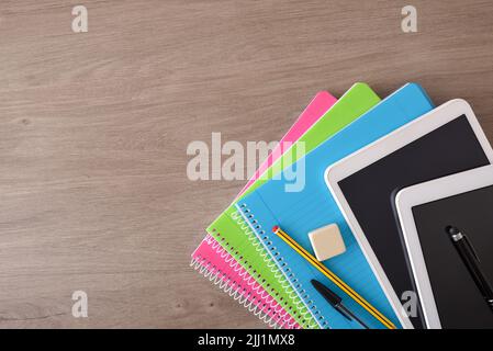 Concetto di apprendimento scolastico con libri elettronici su quaderni di carta su scrivania di legno. Vista dall'alto Foto Stock