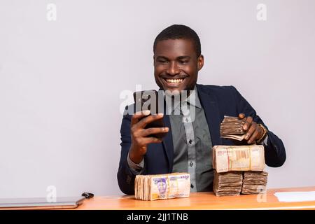 felice uomo d'affari africano con un sacco di soldi utilizzando un telefono Foto Stock