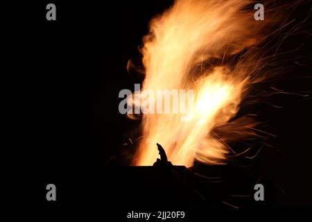 Fiamme di fuoco e scintille da legna che brucia in un camino esterno di metallo di notte contro un cielo scuro Foto Stock