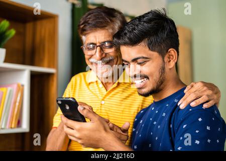 Sorridente nipote che mostra la nuova applicazione sul telefono cellulare a nonno a casa - concetto di social media, navigare in internet e cyberspazio Foto Stock