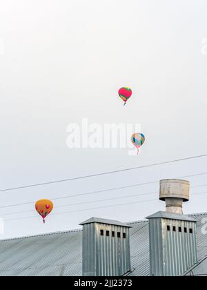 Palloncini multicolore volano nel cielo sopra il tetto di metallo di una casa, foto verticale Foto Stock