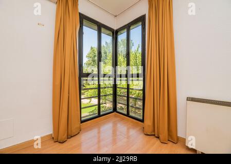 Finestra di una casa all'angolo di una stanza con finestre in alluminio nero e tende color senape Foto Stock