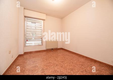 Camera vuota con pavimento in gres rosso, finestra in alluminio con barre e radiatore in alluminio Foto Stock