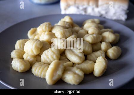 Piatto grigio contenente una generosa porzione di gnocchi di patate appena cotti. Foto Stock