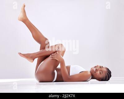 Lavorare su di me in modo coerente. Una giovane donna che si trova a terra con le gambe sollevate su uno sfondo studio. Foto Stock