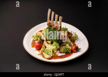 Lamsrack e verdure fresche servite su un piatto. Tutto su sfondo nero Foto Stock