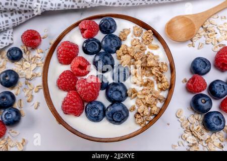 Servire una porzione di yogurt con lampone di mirtillo e fiocchi di avena in un recipiente di legno pronto per essere servito. Alimento sano per concetto di dieta. Frutta muesl Foto Stock