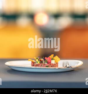 Una bella tartara di tonno appena preparata con verdure dolci/acute, maionese di lime, vinaigrette orientali e nori chips. Con su un piatto bianco. Foto Stock