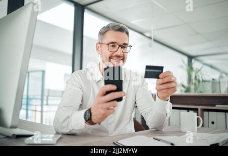 Im comprando più azioni. Un uomo d'affari maturo seduto da solo nel suo ufficio e usando il suo cellulare per il banking online. Foto Stock