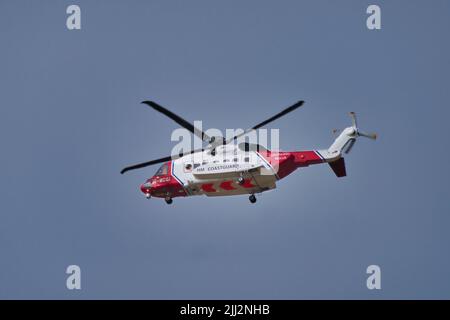 Un elicottero rosso e bianco HM Coastguard Sikorsky S-92A in volo contro un cielo blu grigio. Foto Stock