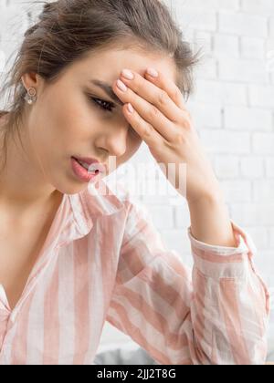 Giovane donna con grave mal di testa. Tiene la fronte e cerca di affrontare il dolore. Foto verticale in primo piano. Foto Stock