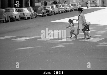 Rimanendo in città 26 luglio 1967 la mamma vestita di cappotto bianco, abito scuro e scarpe bianche attraversa un passaggio pedonale su una strada nel centro di Örebro con due bambini a ogni mano. Il ragazzo è vestito con pantaloni corti bianchi, t-shirt a righe, calzini scuri e sandali bianchi e la ragazza ha un cappuccio velista bianco sulla testa, cappotto a scacchi, mutande bianche, calze bianche e scarpe nere. Foto Stock
