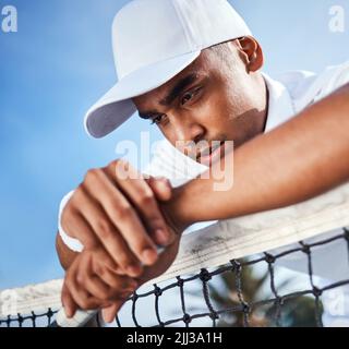 Dai, mettiti insieme. Un bel giovane uomo che si appoggia su una rete da tennis e che si sente deluso dopo la pratica. Foto Stock