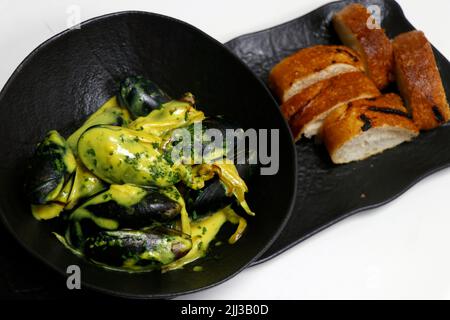 cozze nere cotte in salsa cremosa allo zafferano, servite con pane croccante Foto Stock