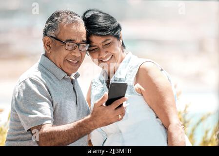 Rimanere in contatto da lontano. Una coppia anziana che usa un telefono in natura. Foto Stock