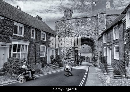 Due scooter per la mobilità vengono condotti verso l'arco Landgate a Rye, Sussex orientale Foto Stock