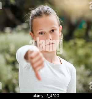 Appena no. Una bambina adorabile che mostra i pollici giù mentre si levano in piedi fuori. Foto Stock