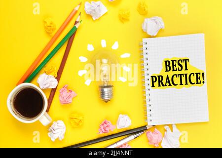 Concetto di business e istruzione. Su sfondo giallo, una tazza di caffè, una lampadina, matite, un taccuino con l'iscrizione - BEST PRACTICE Foto Stock