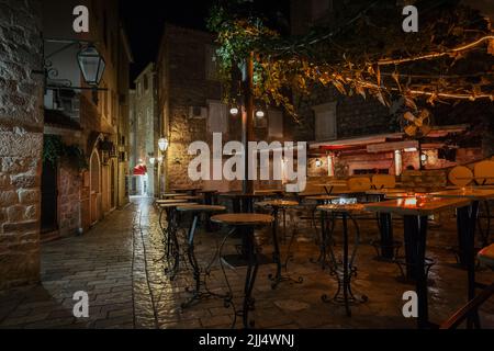 Strada vuota terrazza caffè con tavoli e sedie in una città vecchia di Budva di notte, Montenegro. Foto Stock