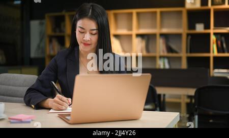 Donna d'affari asiatica executive che usa il computer portatile e scrive il suo piano d'affari sul notebook Foto Stock