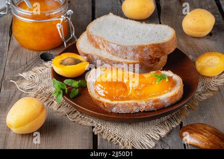 Toast di pane con marmellata di albicocche e frutta fresca con menta su tavola di legno. Foto Stock