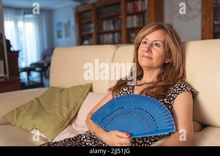 Donna seduta sul divano della sua casa e sudante dalle alte temperature d'estate. Foto Stock
