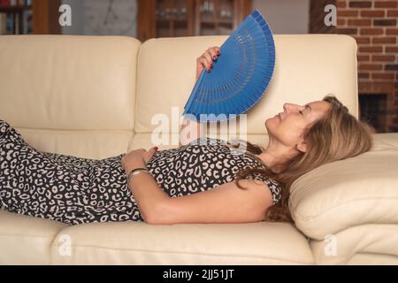 Donna anziana sdraiata sul divano della sua casa e che si abbraccia per combattere il calore estivo. Foto Stock