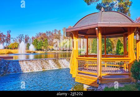 Il bellissimo gazebo in legno sul lago con piccola cascata e fontane sullo sfondo, Mezhyhirya, Ucraina Foto Stock