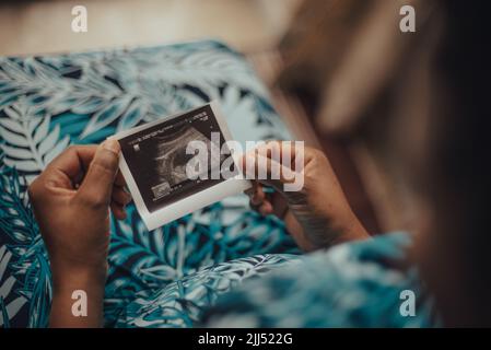 Una donna incinta seduta con un sonogramma seduta al chiuso Foto Stock