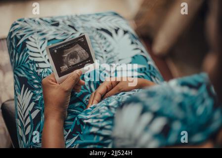 Una donna incinta seduta con un sonogramma seduta al chiuso Foto Stock