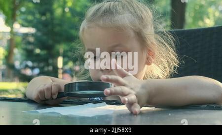 La bambina guarda con attenzione nella lente al sale. Primo piano della ragazza bionda sta studiando i cristalli di sale mentre la guarda attraverso la lente d'ingrandimento Foto Stock