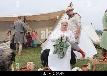 Vichingo contadino cucire a mano un indumento con accampamento sullo sfondo. Fayre verde Upholland, Lancashire, Inghilterra 23-07-2022 Foto Stock