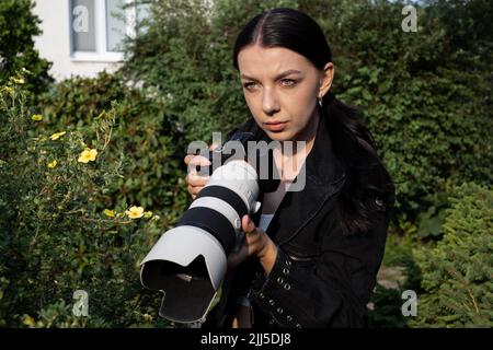 Giovane donna Paparazzi fotografo cattura una foto. Sospettosamente gelosa moglie Detective Spy utilizzando Una fotocamera Big Professional. Foto Stock