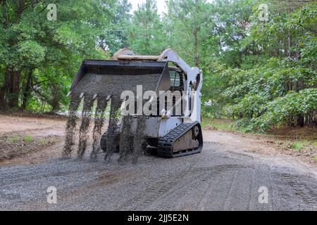 Il trattore Bobcat si muove e scarica la ghiaia sul vecchio sito di ricostruzione stradale Foto Stock