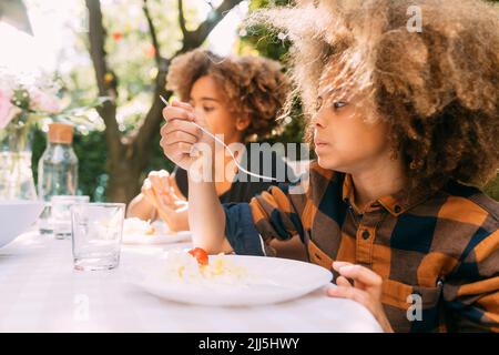 Ragazzo con la sorella che mangia il pranzo al tavolo da pranzo in cortile Foto Stock