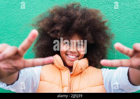 Sorridente ragazza gesturante segno di pace di fronte al muro Foto Stock