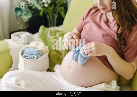 Donna incinta che tiene gli stivaletti del bambino del uncinetto sullo stomaco nel paese Foto Stock