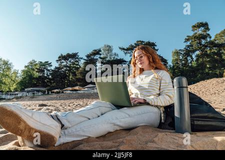 Donna e-learning su laptop in spiaggia Foto Stock