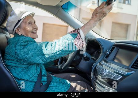 Donna anziana felice che regola lo specchietto retrovisore in auto Foto Stock